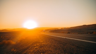 A scenic desert road stretching ahead with an RV cruising along at golden hour.