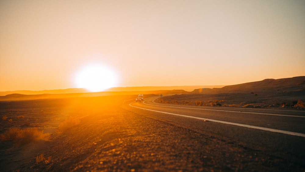 the sun is setting over a desert road