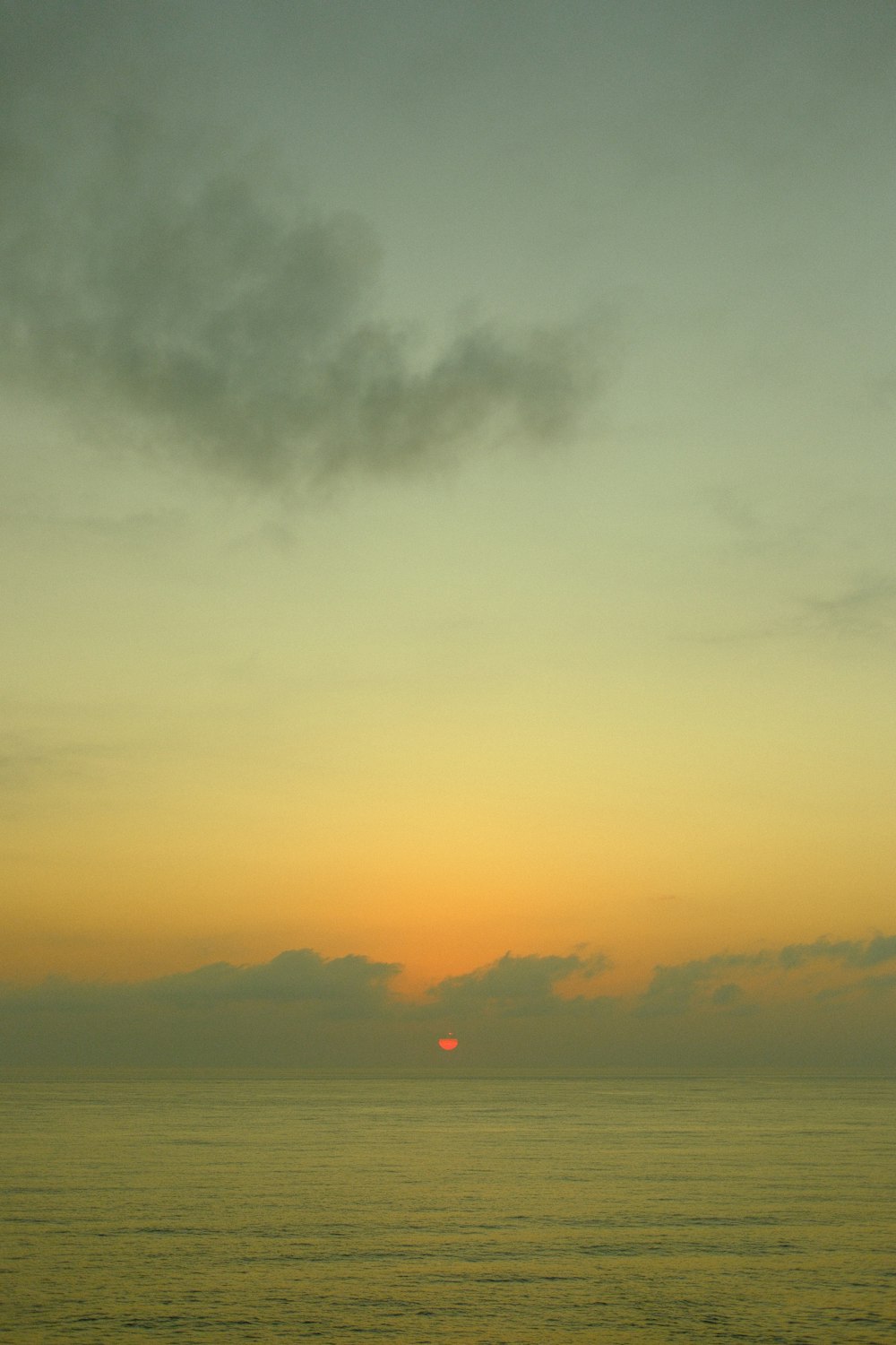 the sun is setting over the ocean on a cloudy day