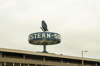 A large circular sign with partially visible letters, positioned above a building. The sign is supported by a central pole, and there is a solar panel or similar structure on top.