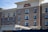 A multi-story hotel building with brick and beige stone exterior featuring numerous windows. Red signage at the top reads 'Hampton Inn & Suites'. The foreground shows part of a vehicle, likely a bus or van.