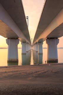 A completed civil infrastructure project showing a sturdy concrete bridge over a river at sunset.