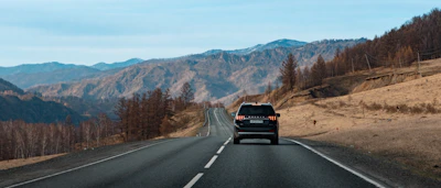 A sleek armored SUV navigating a winding mountain road under a brooding sky in the Andes.