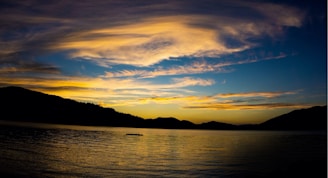 A wide-angle shot of a vibrant sunset over rolling hills and a calm lake.