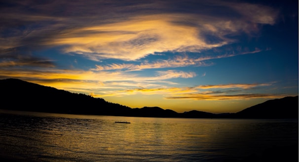 A wide-angle shot of a vibrant sunset over rolling hills and a calm lake.