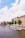 A scenic view of a canal lined with bicycles and historic buildings. Several tour boats are cruising on the water, and the sky is dotted with fluffy white clouds. Trees add greenery along the canal's edge, contributing to the picturesque atmosphere.