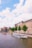 A scenic view of a canal lined with bicycles and historic buildings. Several tour boats are cruising on the water, and the sky is dotted with fluffy white clouds. Trees add greenery along the canal's edge, contributing to the picturesque atmosphere.