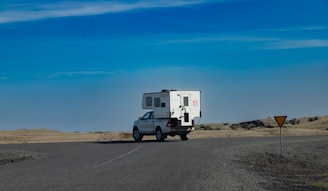 A sturdy tow truck pulling a camper on a sunny day along a rural road.