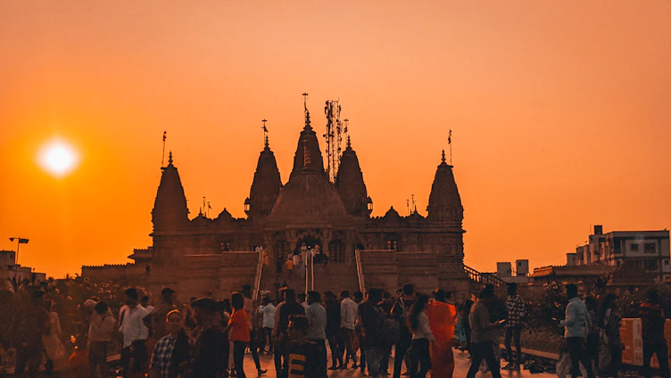 A serene photo of a temple with devotees gathered in prayer during sunset.