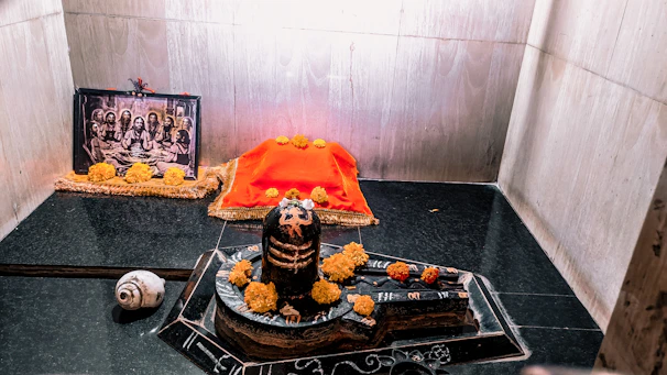 Brass shivling placed on a traditional wooden altar with marigold flowers around.
