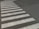 A crosswalk with white stripes is painted on a paved road surface. The paint appears slightly worn and the road is dark, possibly asphalt. The crosswalk forms a distinctive pattern against the background.