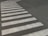 A crosswalk with white stripes is painted on a paved road surface. The paint appears slightly worn and the road is dark, possibly asphalt. The crosswalk forms a distinctive pattern against the background.