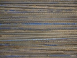 Rusty rebar rods are stacked in an orderly parallel arrangement, displaying a mixture of earthy brown and metallic blue-gray tones.