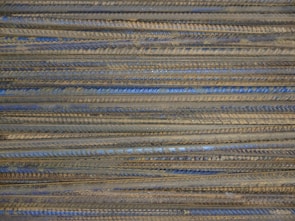 Rusty rebar rods are stacked in an orderly parallel arrangement, displaying a mixture of earthy brown and metallic blue-gray tones.