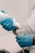A person wearing blue gloves is applying a gel from a bottle onto a medical device, possibly an ultrasound probe, indicating preparation for a medical procedure.