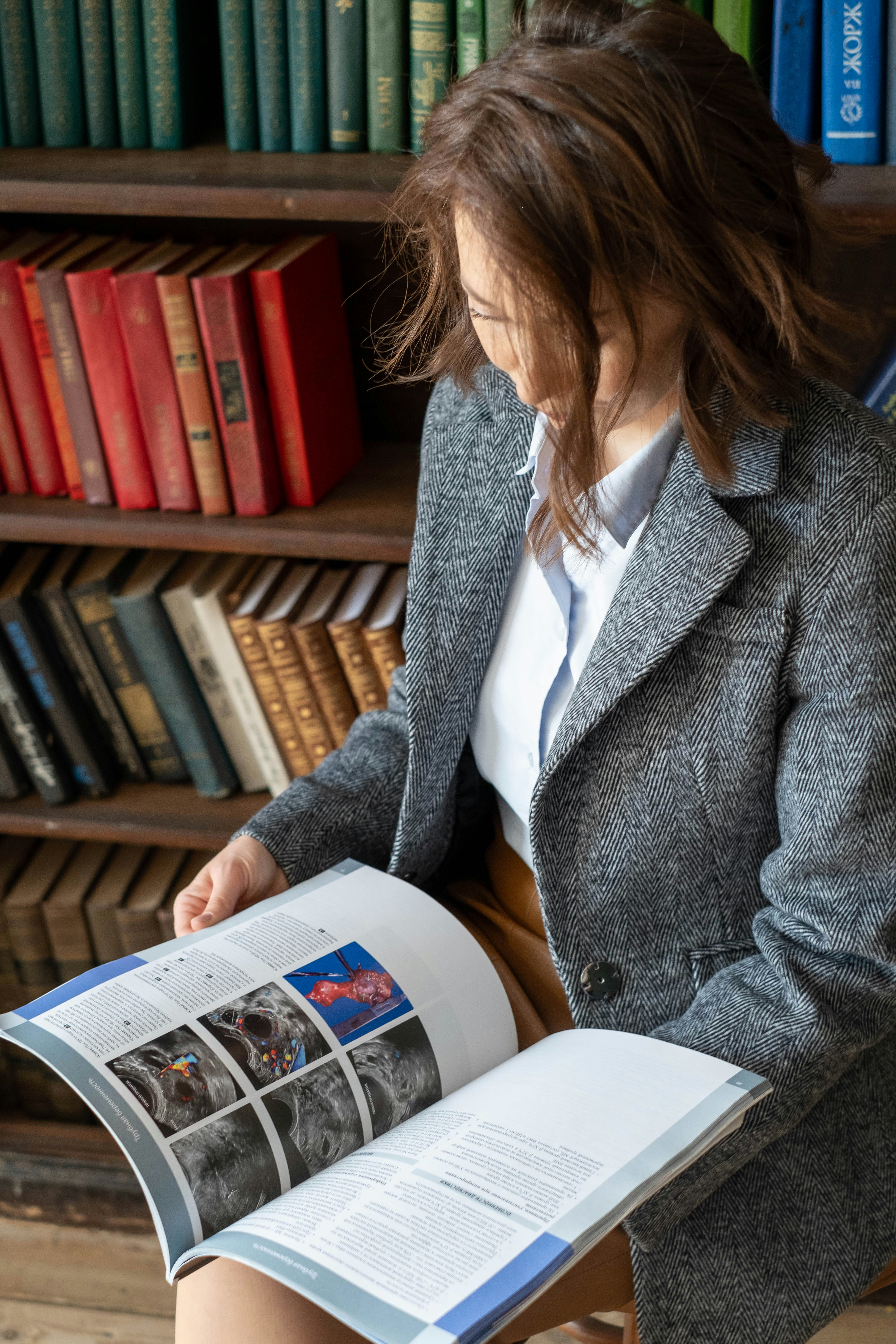 Woman reading a medical textbook in front of a bookshelf.
