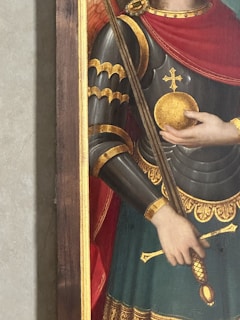 A medieval soldier in ornate armor holds a golden orb and a long staff. The armor is detailed with gold highlights and intricate designs, accompanied by a red cape draped over the shoulders.