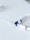 Two syringes lie on a flat white surface, arranged with their needles pointing outward. The syringes have a clear body and one features a blue rotary valve in the center.