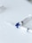 Two syringes lie on a flat white surface, arranged with their needles pointing outward. The syringes have a clear body and one features a blue rotary valve in the center.
