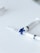 Two syringes lie on a flat white surface, arranged with their needles pointing outward. The syringes have a clear body and one features a blue rotary valve in the center.