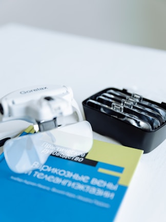 A close-up view of a practical guide book with a blue and yellow cover, along with a prescription lens set and an optical device placed on a flat surface.
