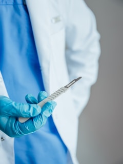 a person in a white coat and blue gloves holding a medical instrument