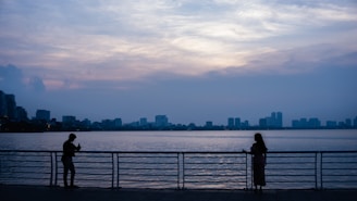 Silhouettes of couples enjoying the calm Tagus River under a fading amber sky.