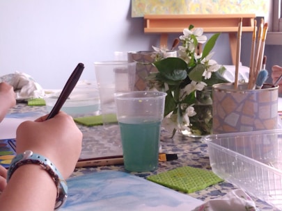 An artist sketching ideas on a notepad surrounded by colorful art supplies.