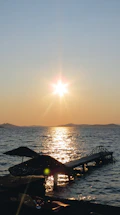 A serene coastal view at sunset with a small wooden pier extending into calm turquoise waters.