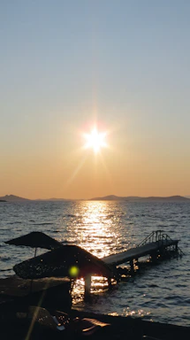 A serene coastal view at sunset with a small wooden pier extending into calm turquoise waters.