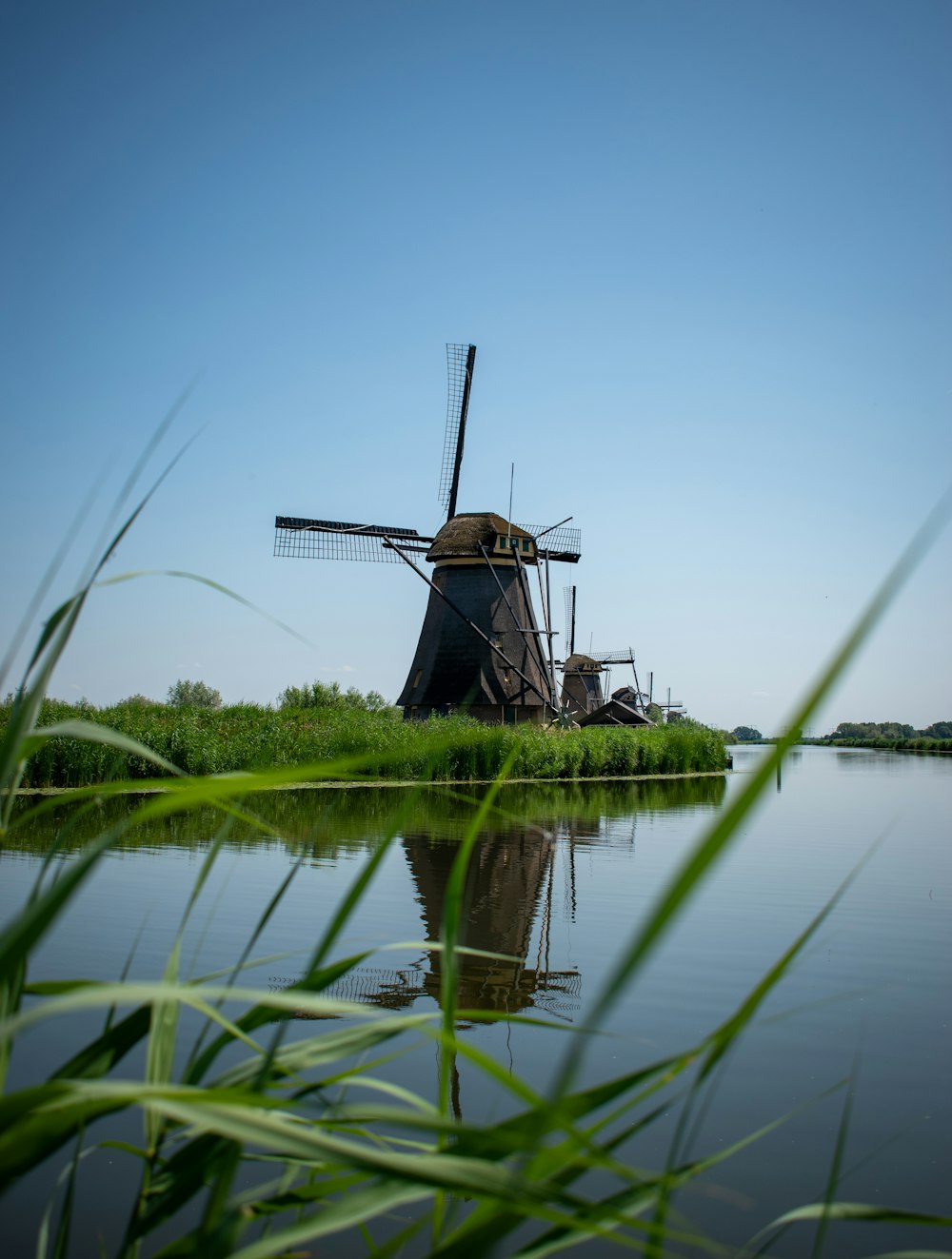 a windmill sitting on top of a river next to a lush green field