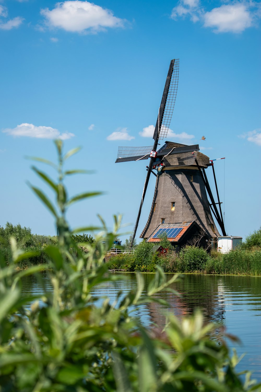a windmill sitting on top of a river next to a lush green field