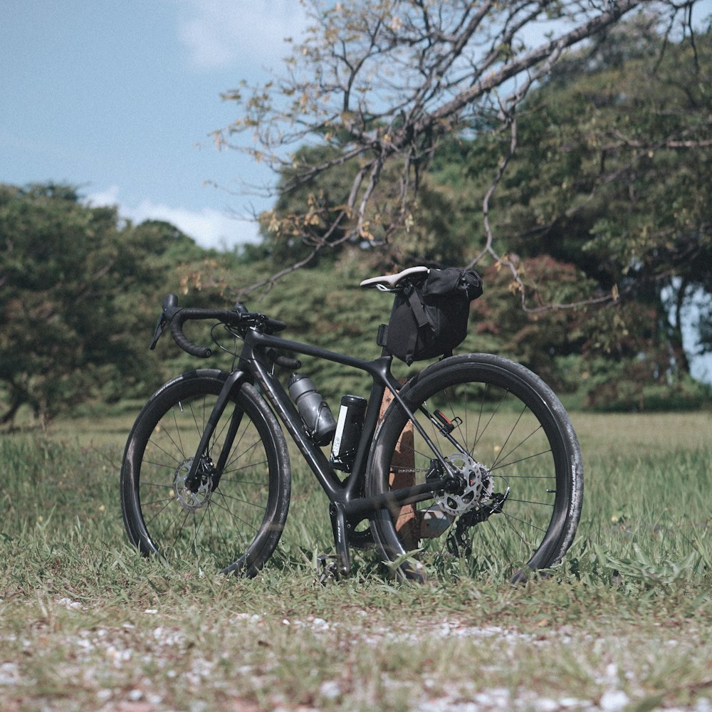 a bicycle parked in a field with a backpack on the back of it