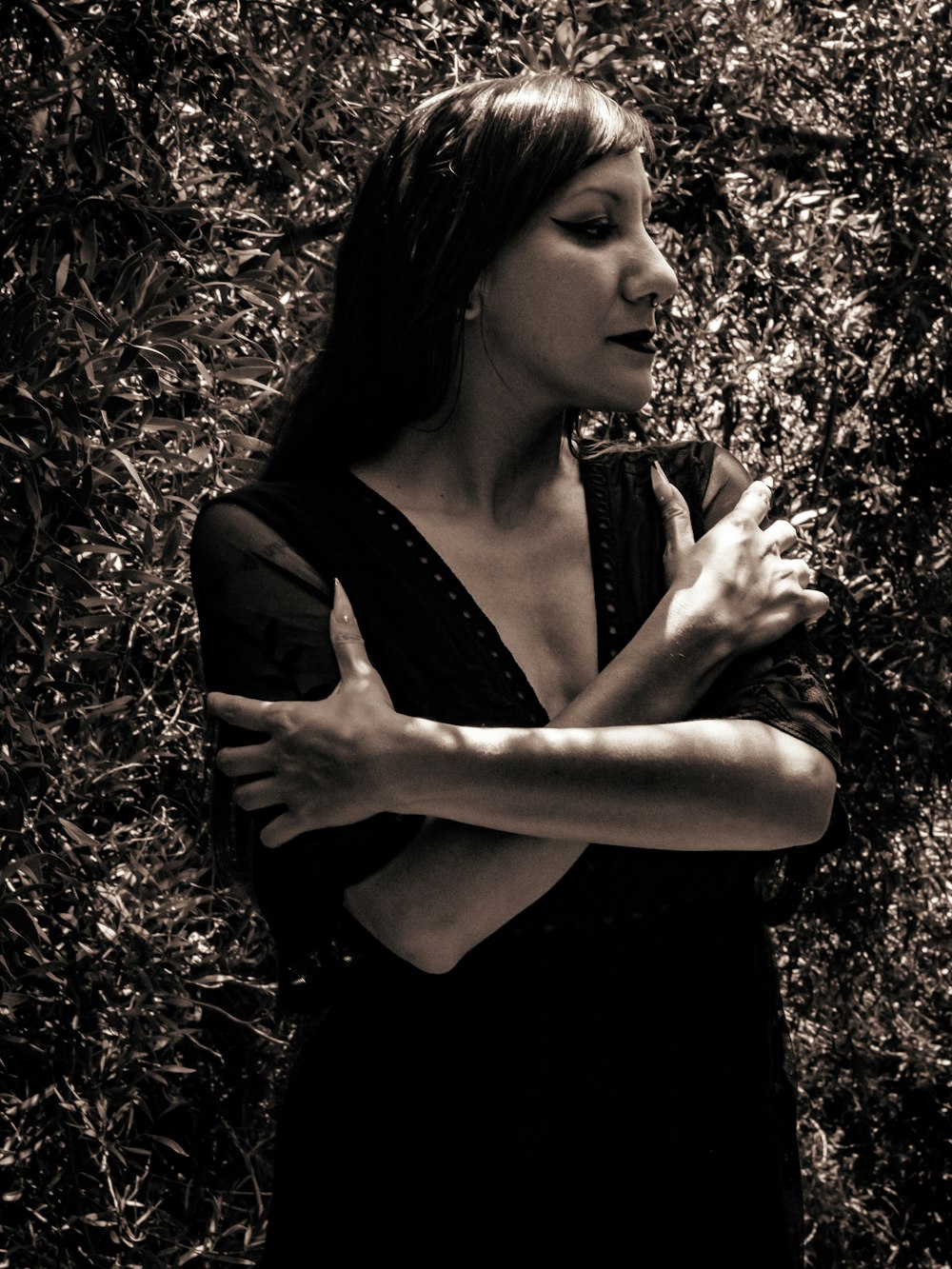 a woman standing in front of a bush with her arms crossed