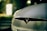 A close-up view of the front of a car featuring the Tesla logo, with a blurred background illuminated by soft, warm lighting.