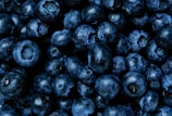 A close-up view of multiple ripe blueberries with a dark, rich blue color. The berries are tightly clustered, showcasing their round shape and slightly glossy texture.
