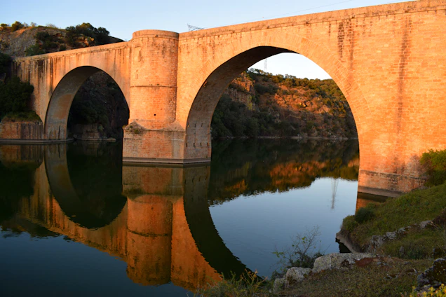 A warm, sunlit bridge arching over a calm river, symbolizing connection and heritage.