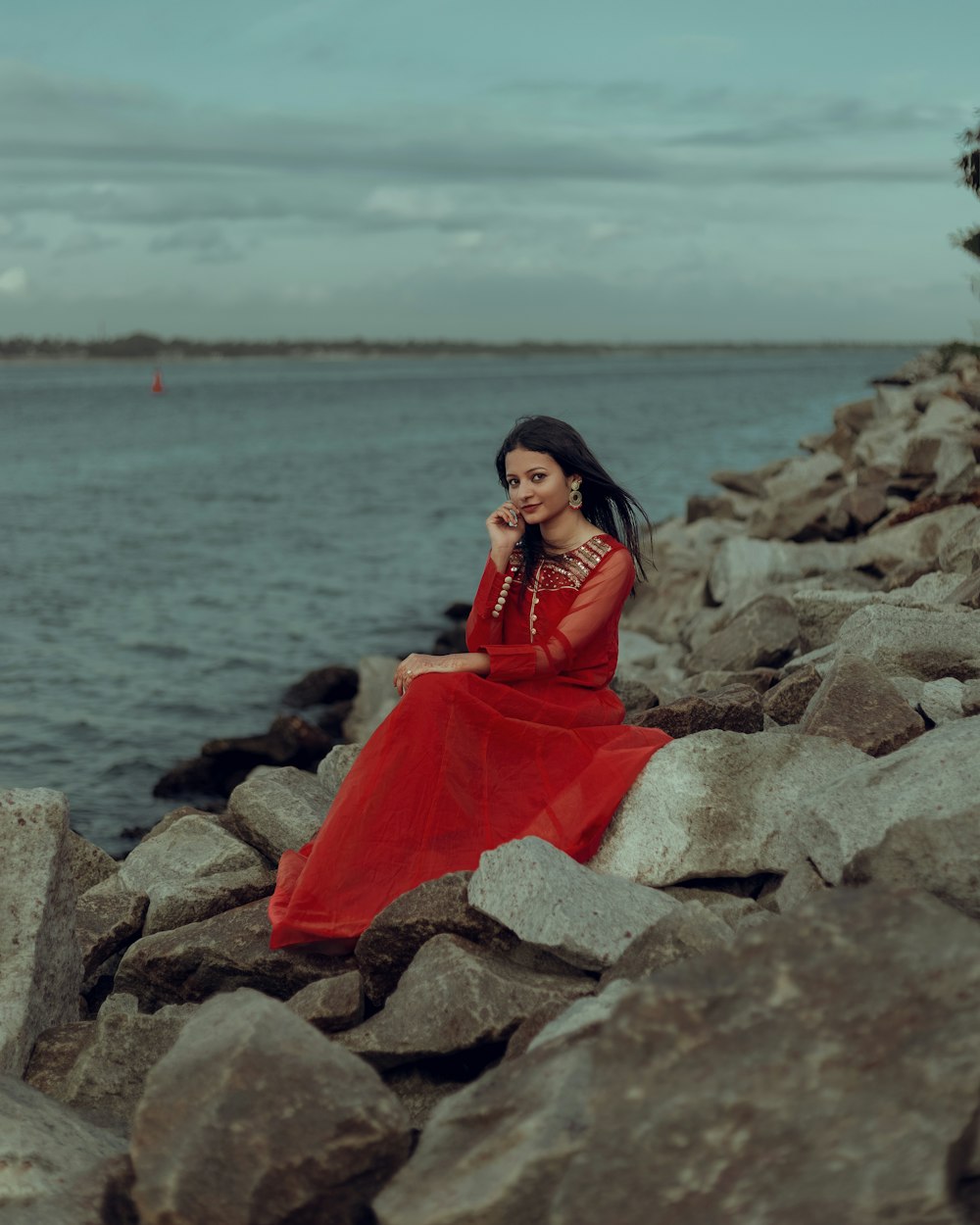 a woman in a red dress sitting on rocks by the water