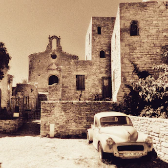 A faded sepia photograph of a historic village street lined with old trees and stone houses.