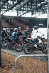 A group of motocross riders preparing their bikes in a dirt track pit area.