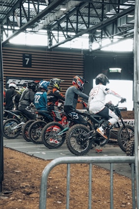 A group of motocross riders preparing their bikes in a dirt track pit area.