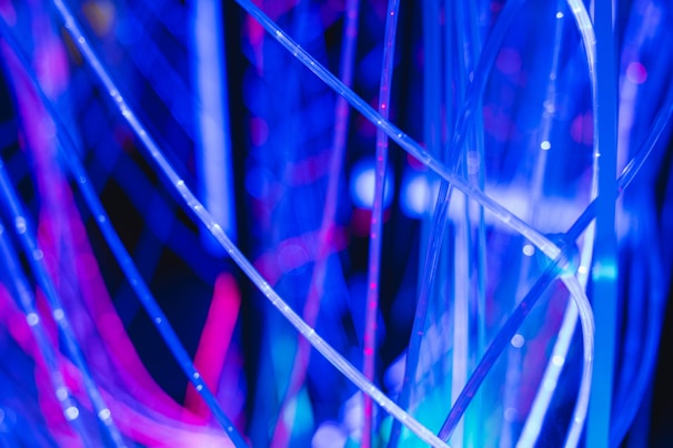 Brightly illuminated translucent fibers intertwine against a dark background, with vibrant blue and pink hues creating a luminous and abstract pattern.