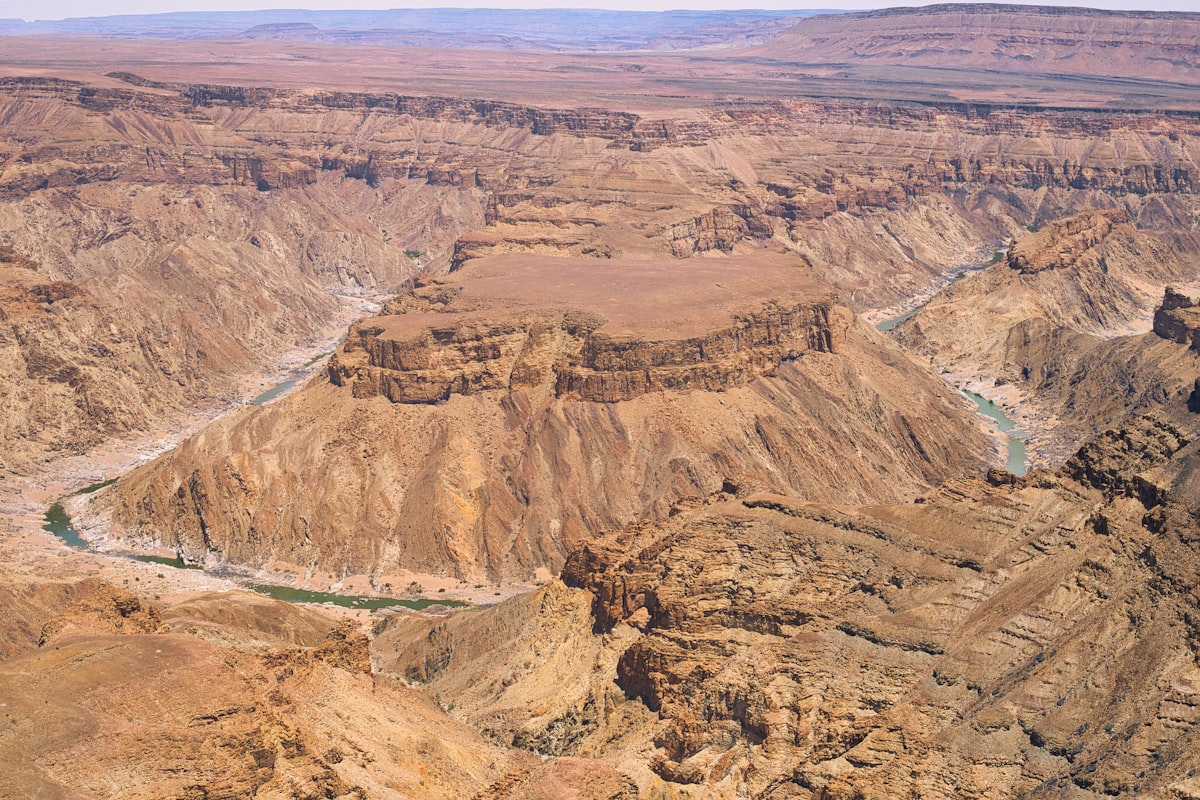 Aerial view of a vast arid canyon with a thin river winding between layered brown rock terraces