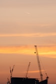 Sunset view over a construction site showing cranes silhouetted against the sky
