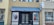 The image features the entrance of a building with a dark double door flanked by two large posters displaying individuals. Above the entrance is a blue awning with 'WRAL NEWS FAYETTEVILLE' written on it. The building is made of light brown bricks and has a modern appearance.