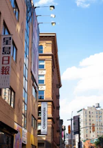 Several multi-story buildings with signs in multiple languages line a city street. The sky is clear with scattered clouds. One prominent sign reads 'Ceremonia', while others feature Asian characters.