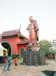 A towering bronze statue of a historical figure standing proudly in a sunlit plaza.