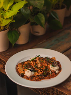 A rustic wooden table displaying a variety of ravioli flavors with roasted eggplant and peppers, surrounded by fresh ingredients.