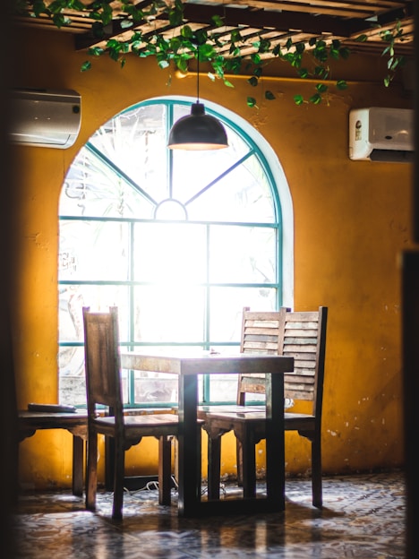 A cozy dining room featuring a vintage solid wood table surrounded by upholstered linen chairs and a rattan bench bathed in warm natural light.