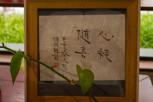 Warm terracotta-hued calligraphy artwork displayed on a sun-drenched wooden table.